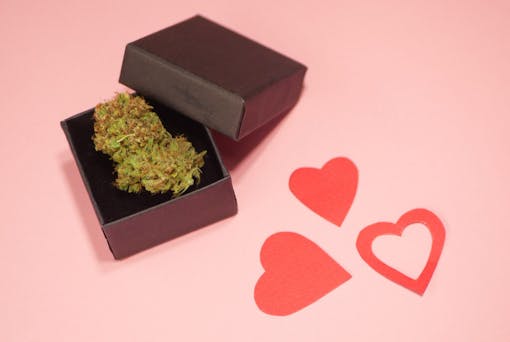 jewelry box with weed nugget inside on pink background. Three red heart cutouts next to box