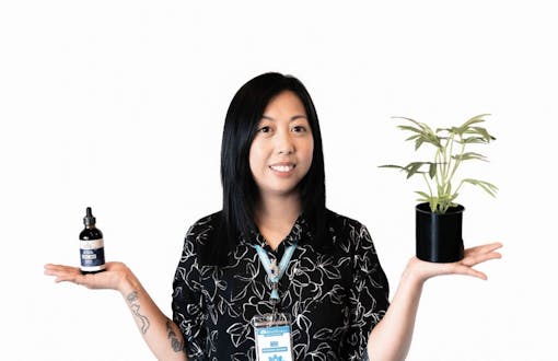woman in dark shirt with tincture in one hand and hemp plan in other hand