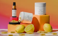 image of several white containers of gummies, on short orange pedestals. sliced lemons rest at bottom of pedestals. background fades from orange to purple, going from top to bottom