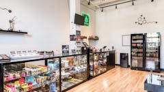 shop interior seen with a row of glass cases, blond wood floors and white walls. on the right side of the frame, we see two stocked beverage cases.