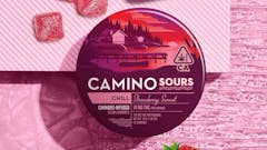 round red tin with illustration of a dock on a lake on it. Package is labeled "CAMINO SOURS CHILL Strawberry Sunset. 10mg per serving." Tin sits on a pink tabletop with three red square gummies above it