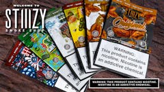 assorted packages of blunt wraps with illustrated designs fanned out like cards. each one has a large warning label noting that the products contain nicotine. Text in upper left reads "Welcome to STIIIZY Smoke Shop."