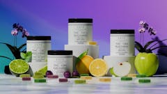 four white jars of gummies from the brand Rare staged on short white pedestals against a magenta background. assorted gummies and slices of fruit are scattered about in front of the gummies