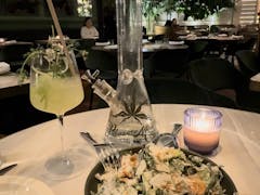 indoor place setting, seen from diner's position: a salad, a candle, a yellow cocktail in a wine glass and a glass bong