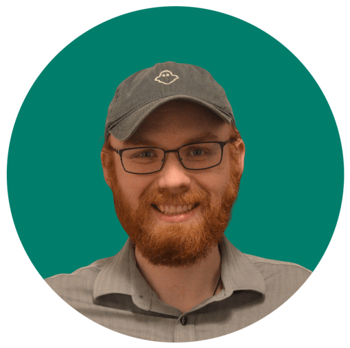 smiling portrait photo of man in glasses and grey cap against an aquamarine background