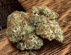 two big marijuana nugs resting next to each other, almost in the shape of two lungs. nugs are bright green and shot through with some dull orange hairs. nugs are sitting on a wooden surface