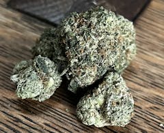 one enormous and very dense marijuana nug in various shades of green, with two similarly-dense and smaller nugs in front of it, all sitting on a wooden table