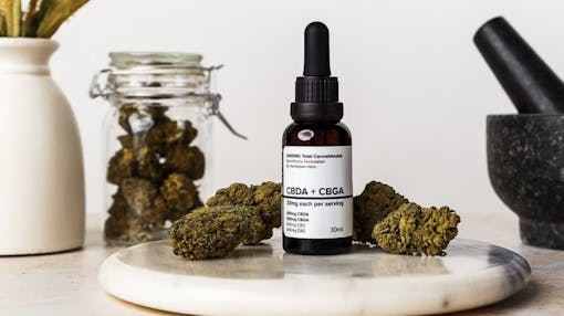 A dropper bottle of Hometown Hero's CBDA tincture with nugs staged around