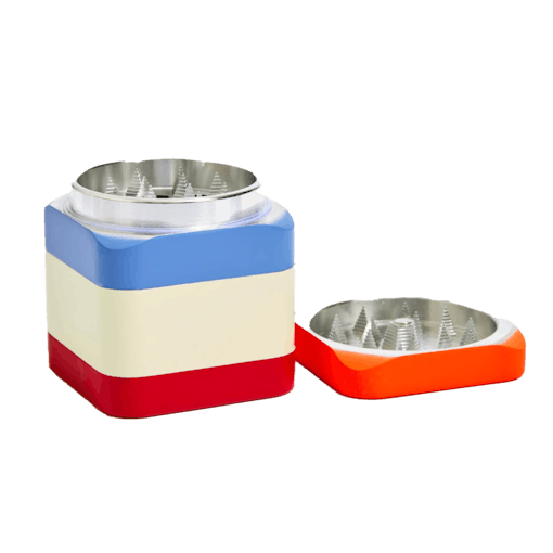 A metal herb grinder with its top off and sitting to the side is shown against a white background. The grinder body is colored blocked with three bands of light blue, cream white, and red, while the top portion is orange in color. One of our best products for July 4th weekend.