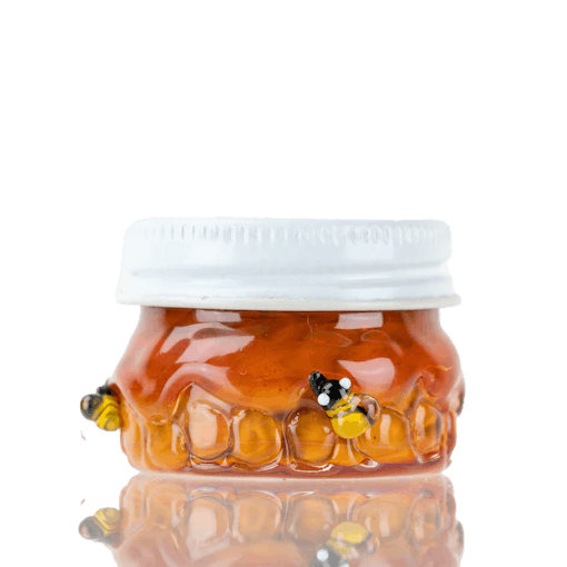 A small glass jar for containing concentrates with a design showing small bees on a honeycomb with honey over-following against a white background, one of our picks for the best products for Oil Day
