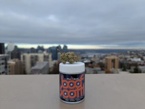 A 3.5g jar of Boofscotti from Fire Bros is photographed in front of the Seattle city skyline, one of our best strains in Washington.